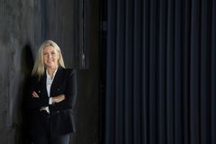 Tina Hedegaard i sort jakke står smilende ved en mørk væg.