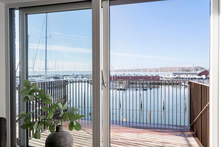 Udsigt%20over%20en%20marina%20fra%20en%20balkon%20med%20glidende%20glasd%F8re%2C%20b%E5dst%E6nger%20og%20bl%E5%20himmel%20i%20baggrunden.