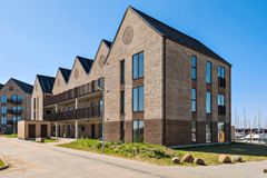 Et moderne lejlighedskompleks med murstensfacade og stejle tage under en klar blå himmel.