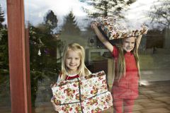 To piger kigger ud af et vindue og holder indpakkede julegaver.