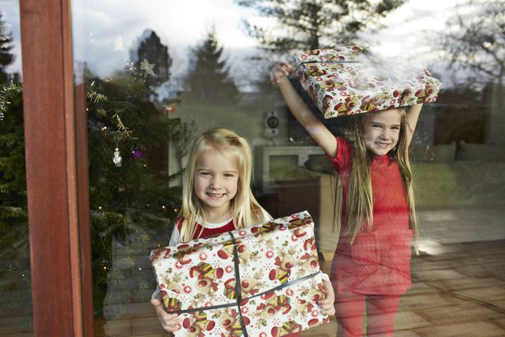 To piger kigger ud af et vindue og holder indpakkede julegaver.