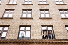 To personer kigger ud af et vindue i en murstensbygning.