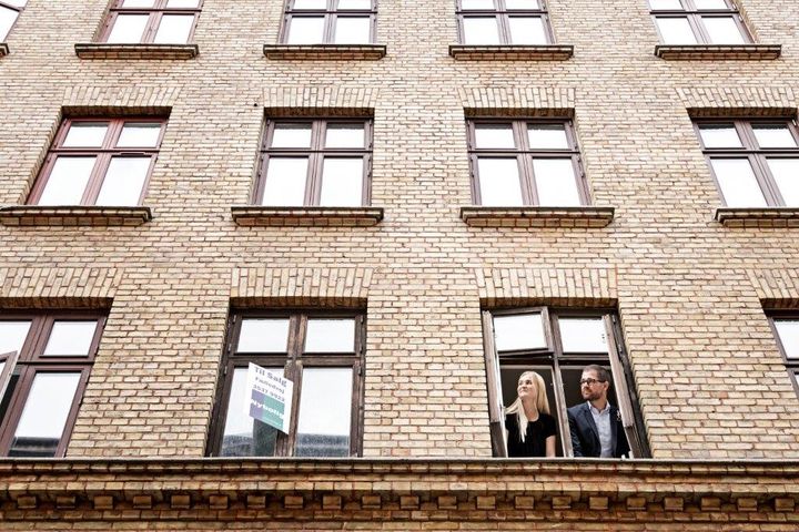 To personer kigger ud af et vindue i en murstensbygning.