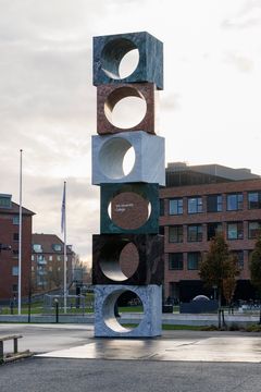 En høj skulptur af stablede stenklodser med runde udskæringer står udendørs foran VIA i Horsens.