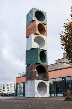 En høj skulptur af stablede stenklodser med runde udskæringer står udendørs foran VIA i Horsens.