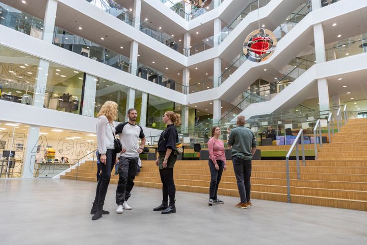 Fem elever fra VIAs læreruddannelse står og taler sammen i atriummet på Campus Aarhus C.